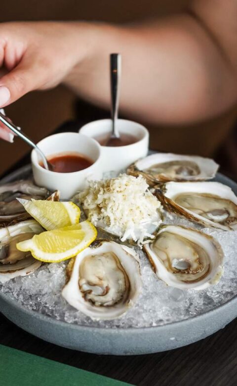 a plate of oysters with dipping sauce and lemon wedges